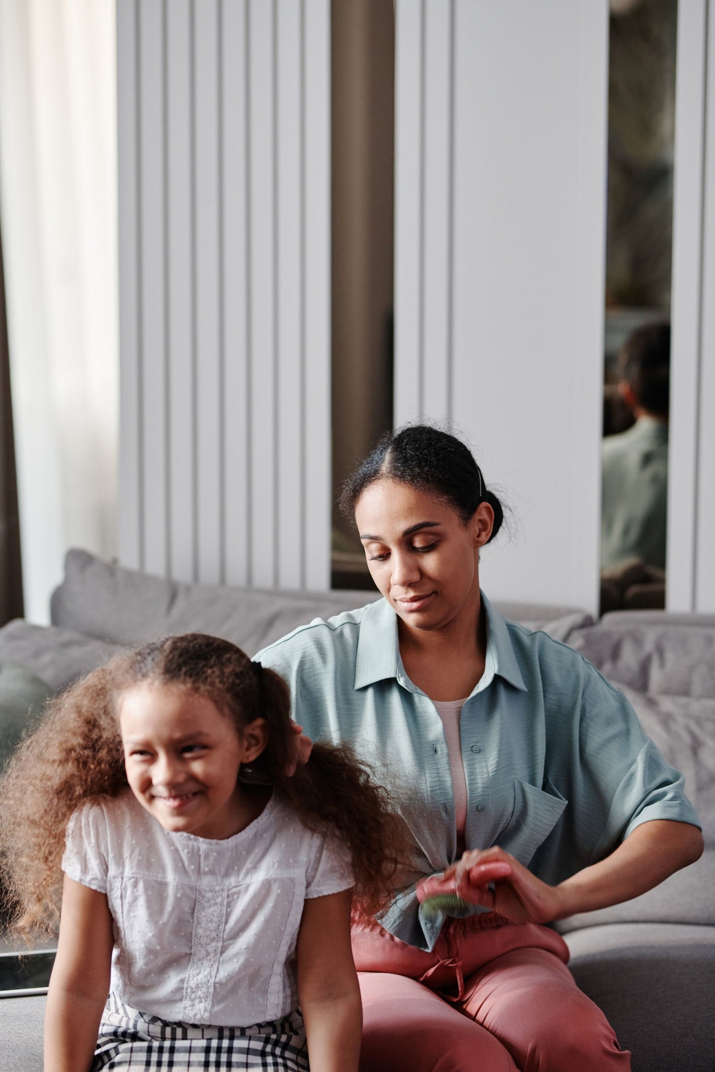 Mother styling her daughter's curly afro-textured hair as part of a back-to-school hair care routine
